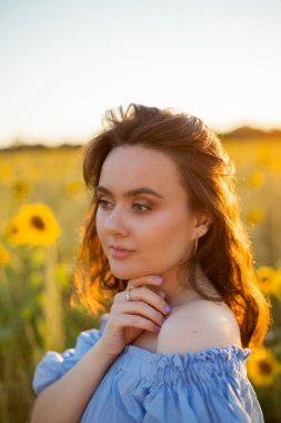 Ayçiçeği tarlasında siyah kıvırcık saçlı güzel bir genç kadın. Şık mavi elbiseli bir manken. Yaz.