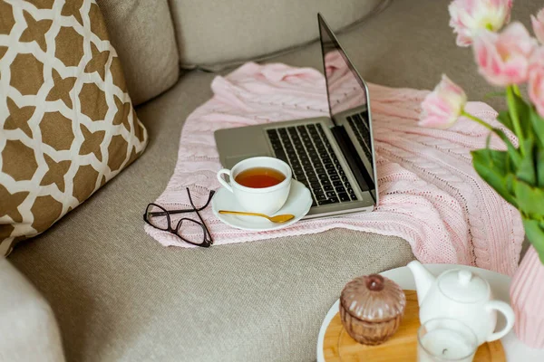 Home cozy office. Work at home. Spring decor. Knitted blanket, bouquet of tulips, hot tea, laptop.