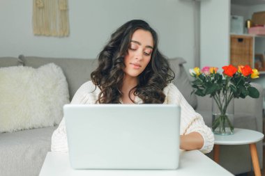 Young dark haired woman works online using laptop. Beautiful model in knitted sweater at home office.