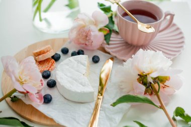 Beautiful breakfast. Fruits, berries, brie cheese, hot tea in mug, bouquet of pink peonies. Spring mood at home.