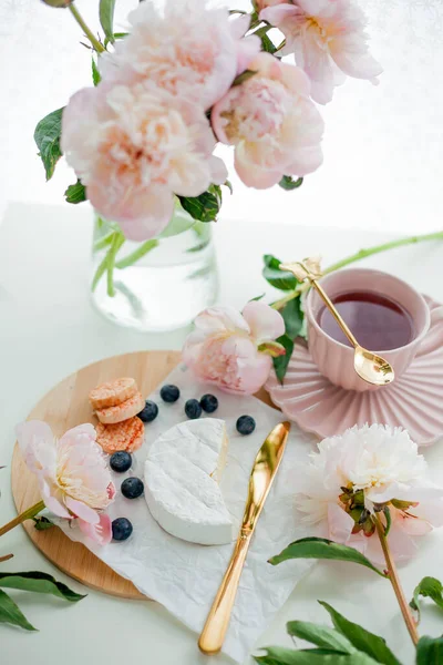 Beautiful breakfast. Fruits, berries, brie cheese, hot tea in mug, bouquet of pink peonies. Spring mood at home.