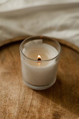 Burning candle on a wooden tray on the bed. Cozy house. Decor.
