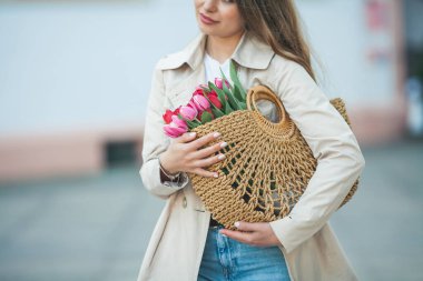 28 yaşında, uzun, bakımlı saçlarıyla genç ve güzel bir kadının bahar portresi elinde bir şehir caddesinde bir buket lale ile bir hasır çanta tutuyor. Tarz modeli