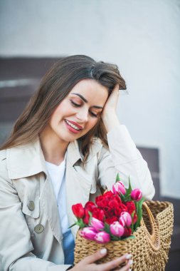 28 yaşında, uzun, bakımlı saçlarıyla genç ve güzel bir kadının bahar portresi elinde bir şehir caddesinde bir buket lale ile bir hasır çanta tutuyor. Tarz modeli