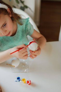 Easter. A cute little girl in bunny ears decorates Easter eggs at the table at home. Spring.
