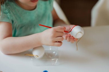 Easter. A cute little girl in bunny ears decorates Easter eggs at the table at home. Spring.