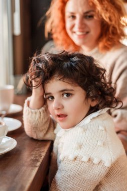Şirin kıvırcık saçlı kızı olan güzel, genç, kızıl saçlı anne rahat bir kafede oturmuş sıcak bir okul içiyorlar. Anneler Günü.