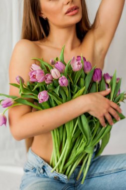 Portrait of sexy beautiful young woman with long hair. Model with a bouquet of lilac tulips on white. Holidays.