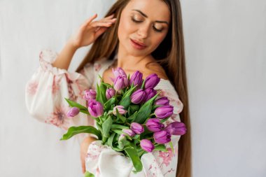 Portrait of sexy beautiful young woman with long hair. Model with a bouquet of lilac tulips on white. Holidays.