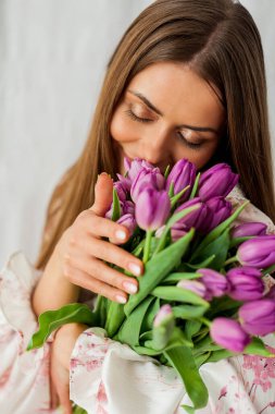 Uzun saçlı, seksi, genç bir kadının portresi. Beyaz üzerinde leylak rengi laleler olan bir model. Tatiller.