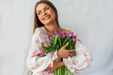 Uzun saçlı, seksi, genç bir kadının portresi. Beyaz üzerinde leylak rengi laleler olan bir model. Tatiller.
