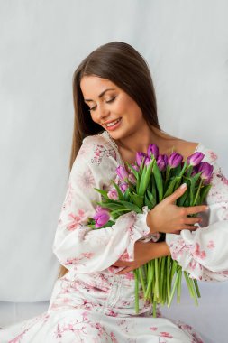 Portrait of sexy beautiful young woman with long hair. Model with a bouquet of lilac tulips on white. Holidays.