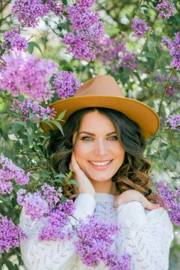 Genç, güzel, koyu renk saçlı bir kadının portresi. Çiçek açan şapkanın yanında mavi gözlü. Kıvırcık saçlı mutlu manken..