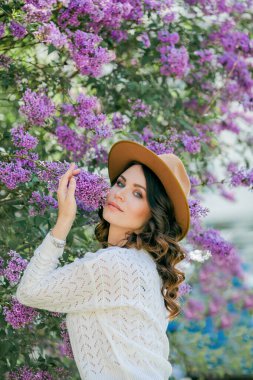 Genç, güzel, koyu renk saçlı bir kadının portresi. Çiçek açan şapkanın yanında mavi gözlü. Kıvırcık saçlı mutlu manken..