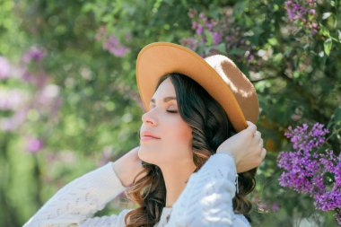 Genç, güzel, koyu renk saçlı bir kadının portresi. Çiçek açan şapkanın yanında mavi gözlü. Kıvırcık saçlı mutlu manken..