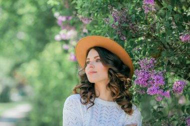 Genç, güzel, koyu renk saçlı bir kadının portresi. Çiçek açan şapkanın yanında mavi gözlü. Kıvırcık saçlı mutlu manken..