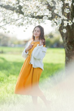 Çiçek açan ağacın yanındaki güzel, koyu saçlı kadının portresi. Bahçede mutlu bir model.