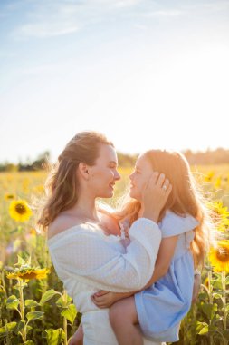 Mom hugs her little daughter. A beautiful young woman with a 4-year-old child in her arms in a sunflower field.