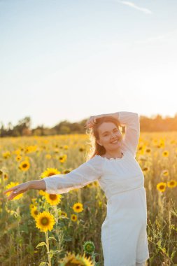 Gün batımında ayçiçeği tarlasında beyaz elbiseli güzel sarışın kadın. Akşam güneşleri.