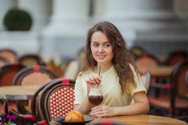 Koyu renk saçlı güzel kıvırcık kadın yaz kafesinde oturur ve kahve kokteyli içer. Sıcak..