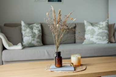 Evin içi rahattır. Mumlar, bir buket çiçek, ahşap sehpanın üzerindeki cam vazoda..