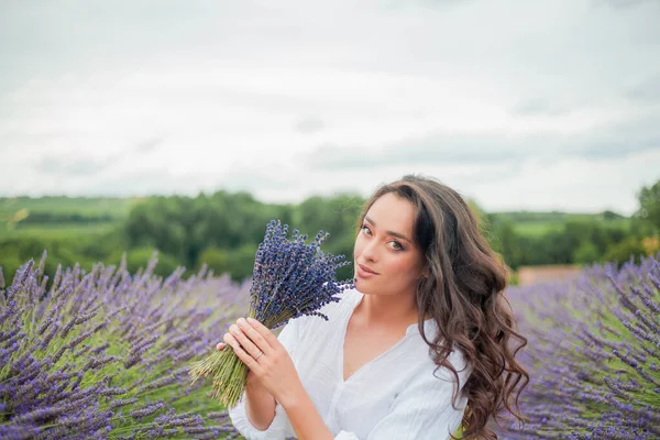Lavanta tarlası. Güzel, siyah saçlı, kıvırcık saçlı, beyaz elbiseli, mor çiçekli bir kadın..