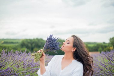 Lavanta tarlası. Güzel, siyah saçlı, kıvırcık saçlı, beyaz elbiseli, mor çiçekli bir kadın..