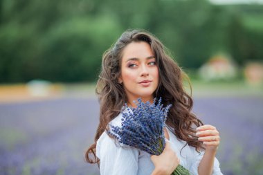 Lavanta tarlası. Güzel, siyah saçlı, kıvırcık saçlı, beyaz elbiseli, mor çiçekli bir kadın..
