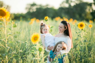 Güzel, genç, siyah saçlı anne kızlarıyla güneşte ayçiçeği tarlasında oynuyor. Aile.