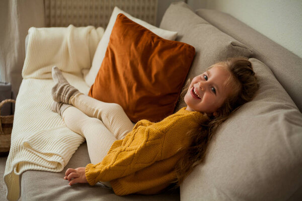 Cute little blue-eyed curly girl 4 years old drinking tea in a cozy house. Autumn.