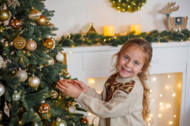 5 yaşında, uzun kıvırcık saçlı ve mavi gözlü sevimli küçük bir kız Noel ağacını süslüyor. Tatillerde. Yeni Yıl.