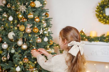 5 yaşında, uzun kıvırcık saçlı ve mavi gözlü sevimli küçük bir kız Noel ağacını süslüyor. Tatillerde. Yeni Yıl.
