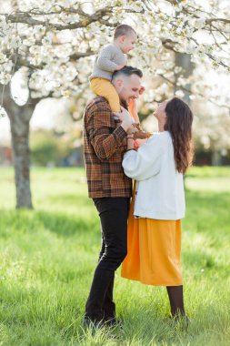 Mutlu genç aile bahar aylarında çiçek açan parkta vakit geçirir. Anne, baba ve küçük oğlu oynuyorlar..
