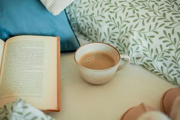 Mug of hot coffee, book, soft slippers on the bed. Breakfast in bed. Cozy home. Winter.