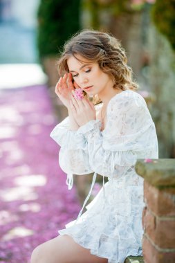 Açık romantik elbiseli güzel sarışın. Avrupa 'da bir kentin çiçek açan sakura ağacının yanında genç bir kadının portresi. Bahar.