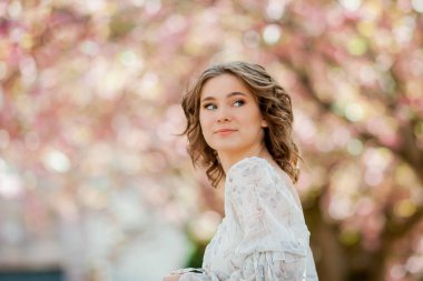 Açık romantik elbiseli güzel sarışın. Avrupa 'da bir kentin çiçek açan sakura ağacının yanında genç bir kadının portresi. Bahar.