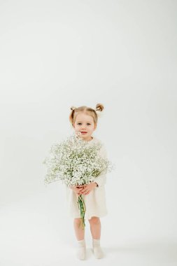 Elinde bir buket beyaz çiçekle 3 yaşında tatlı bir kız annesini Anneler Günü 'nde tebrik ediyor. Mutlu gülümseyen çocuk.
