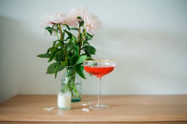 Cam vazoda bir buket pembe şakayık, mumlar, beyaz arka planda tahta sandıkta pembe bir kokteyl..