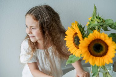 Evinde bir buket ayçiçeğiyle mavi gözlü tatlı kıvırcık kız portresi.