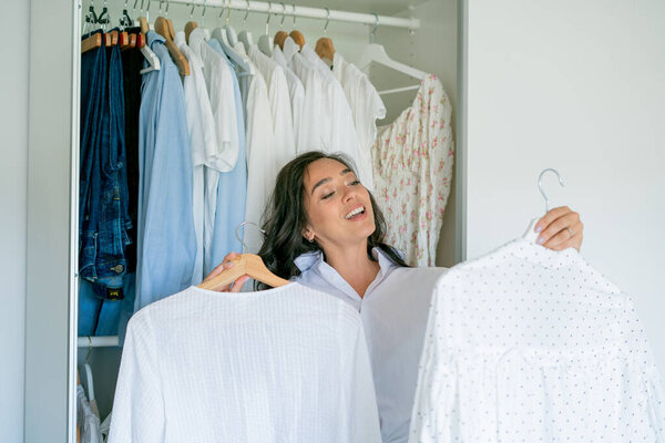 Молодая темноволосая кудрявая красивая женщина разбирает вещи в большом просторном шкафу. Домашняя организация Стирка вещей.