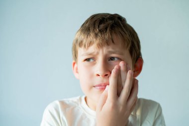 Diş ağrısı. 10 yaşındaki çocuk elleriyle yüzünü tutuyor..