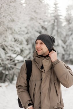 Kış ormanında sıcak kıyafetler içindeki genç bir adamın portresi. Turizm.