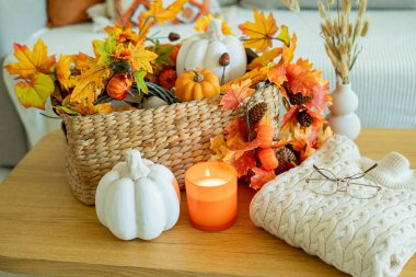 Balkabağı, portakal yaprakları, sepetteki süsler, kanepenin yanındaki ahşap sehpada mumlar. Ev dekoru.