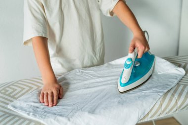 Sevimli 10 yaşındaki çocuk ev ödevi yapıyor ve elbiselerini ütülüyor..