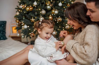 Aile Noel ağacının yanında oturuyor ve hediyeleri açıyor. Kış tatili Tatiller