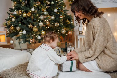 Anne ve küçük kızı Noel ağacının yanında oturup hediyeleri açıyorlar. Kış tatili Tatiller