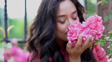 Şehir parkında pembe güllerin yanında güzel siyah saçlı kıvırcık kadın portresi.