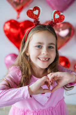 Pembe balonların arka planında kalp gözlüğü takan uzun kıvırcık saçlı tatlı küçük kız. Doğum gününü kutluyoruz. Sevgililer Günü.