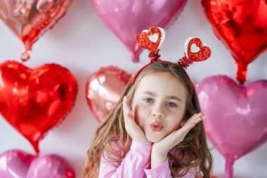Pembe balonların arka planında kalp gözlüğü takan uzun kıvırcık saçlı tatlı küçük kız. Doğum gününü kutluyoruz. Sevgililer Günü.