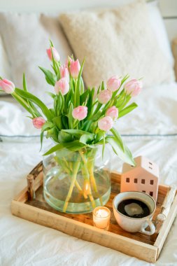 Bahar dekoru, vazoda bir buket lale, tahta tepside sıcak kahve. Yatakta kahvaltı. Yatak odasının içi..